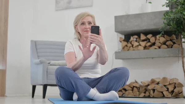 Старуха с помощью смартфона на коврике упражнений дома — стоковое фото