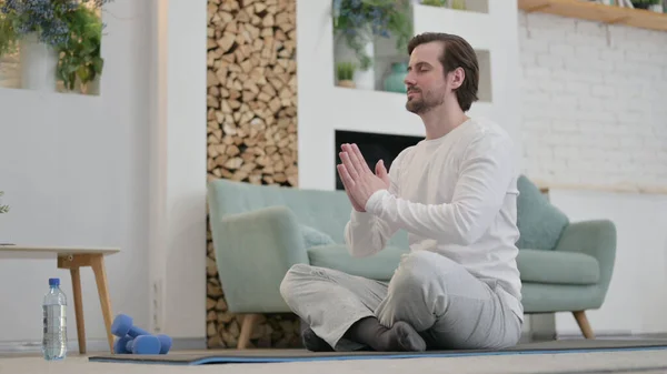 Молодой человек медитирует на тренировочном коврике дома — стоковое фото