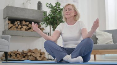 Yaşlı kadın evde meditasyon yapıyor.