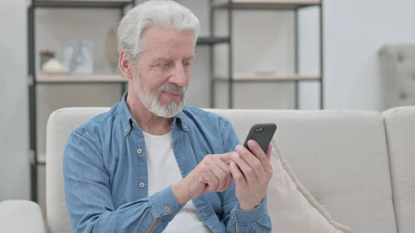 Alter Mann benutzt Smartphone im Sitzen auf Sofa — Stockfoto