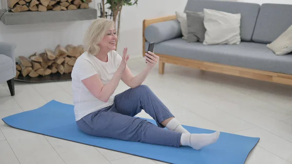 Velha mulher falando em vídeo chamada em Smartphone enquanto sentado no tapete Excercise — Fotografia de Stock