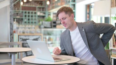 Dizüstü bilgisayarı olan genç adam sırt ağrısı çekiyor. 