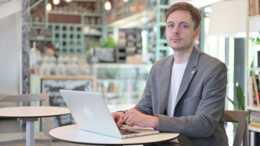 Cafe 'de dizüstü bilgisayar kullanırken kameraya bakan çekici genç adam.