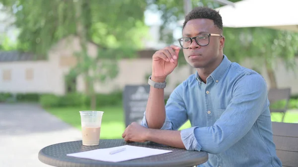 Pensive Afrikaanse man met koffie en documenten, denken in Outdoor Cafe — Stockfoto
