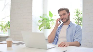 Dizüstü bilgisayarlı genç adam Smartphone 'da konuşuyor 