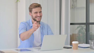 Bilgisayarlı bir adam ofiste kamerayı işaret ediyor.