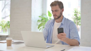 Modern Ofiste akıllı telefon kullanan dizüstü bilgisayarı olan bir adam.