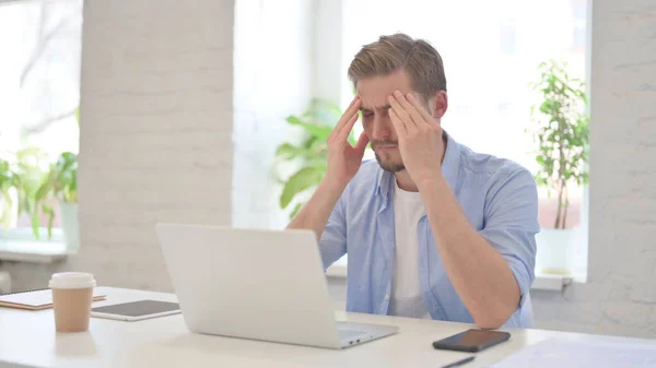 Homem jovem com dor de cabeça no escritório moderno — Fotografia de Stock