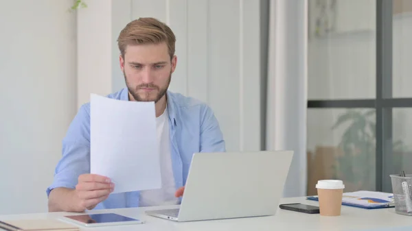 Mann mit Laptop liest Dokumente im Büro — Stockfoto