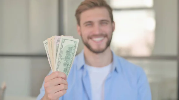 Retrato do jovem sorrindo enquanto oferece dólares — Fotografia de Stock