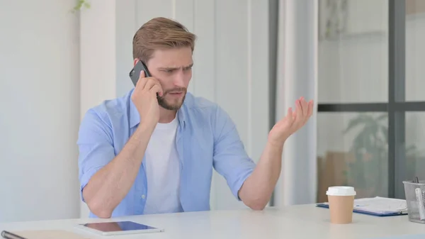 Wütender junger Mann spricht im Büro auf Smartphone — Stockfoto