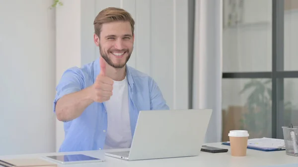 Pulgares hacia arriba por el hombre joven con el ordenador portátil en el trabajo — Foto de Stock