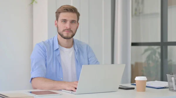 Mann blickt im Büro mit Laptop auf Kamera — Stockfoto