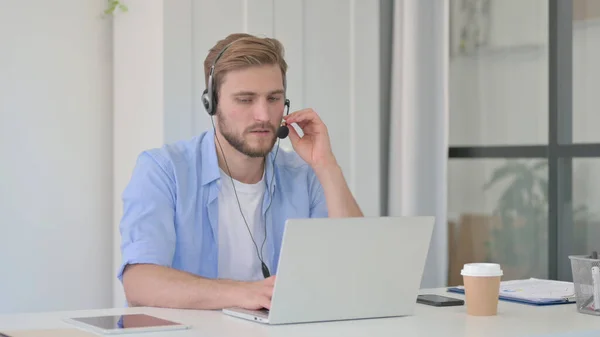 Mann spricht am Headset, arbeitet im Büro am Laptop — Stockfoto