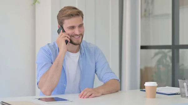 Junger Mann spricht im Büro mit Smartphone — Stockfoto