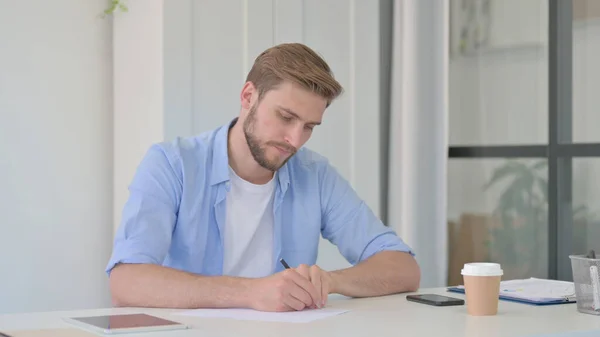 Umsichtiger junger Mann, der auf Papier schreibt und denkt — Stockfoto