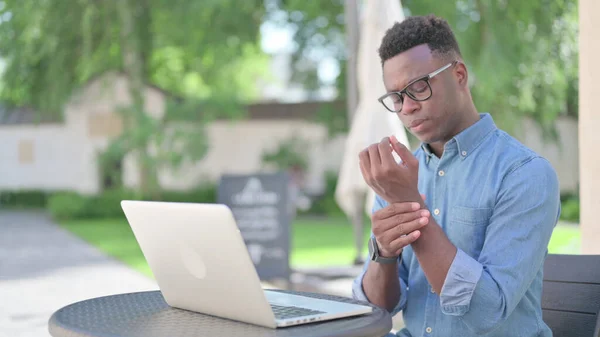 Dizüstü bilgisayarı olan Afrikalı adam bilek ağrısı çekiyor, dışarıda oturuyor. — Stok fotoğraf