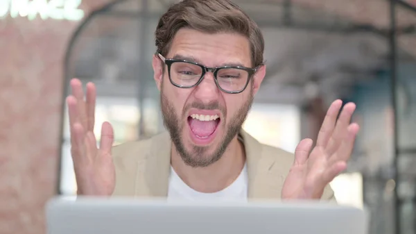 Hombre joven con el ordenador portátil sorprendido en el trabajo — Foto de Stock