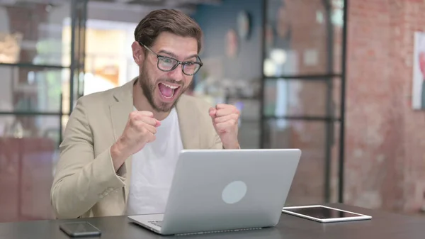 Giovane uomo di successo che festeggia sul computer portatile al lavoro — Foto Stock