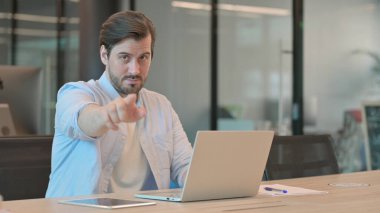 Bilgisayarlı bir adam ofiste kamerayı işaret ediyor.