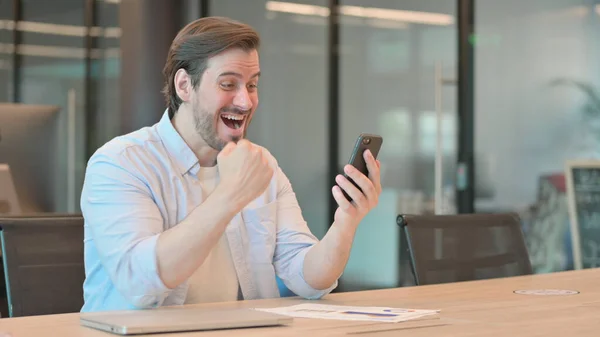 Uomo adulto maturo che celebra il successo sullo smartphone in ufficio — Foto Stock