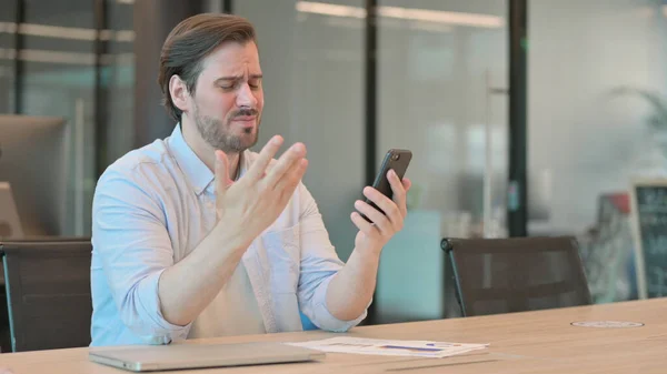 Reifer erwachsener Mann reagiert auf Verlust mit Smartphone im Büro — Stockfoto