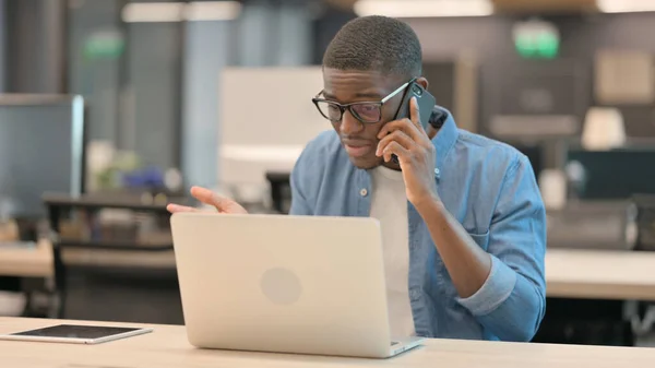 Wściekły Afrykanin rozmawiający przez telefon w pracy — Zdjęcie stockowe