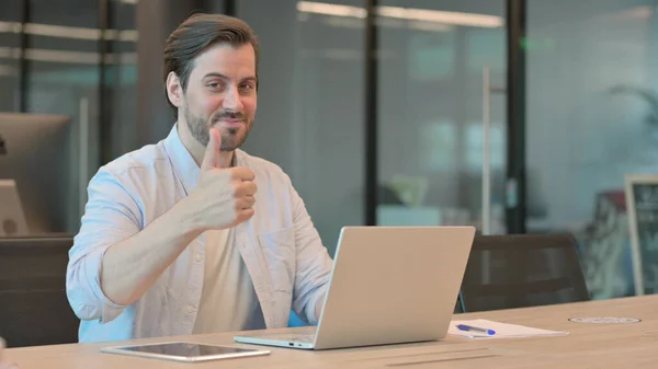 Polegares para cima por homem com laptop no escritório — Fotografia de Stock