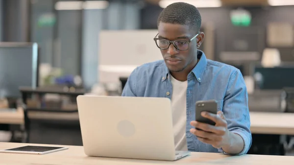 Mladý Afričan používající chytrý telefon v práci — Stock fotografie