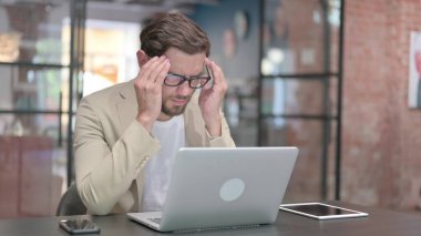 İş yerinde baş ağrısı olan yorgun genç adam. 