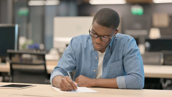 사무실에서 종이에 글씨를 쓰는 열심 히 일하는 젊은 아프리카 남자 — 스톡 사진
