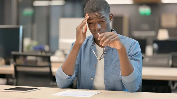 Mladý Afričan s bolestí hlavy, zatímco sedí v kanceláři — Stock fotografie