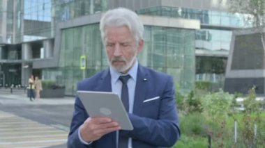 Yaşlı işadamı sokakta yürürken tablet kullanıyor. 