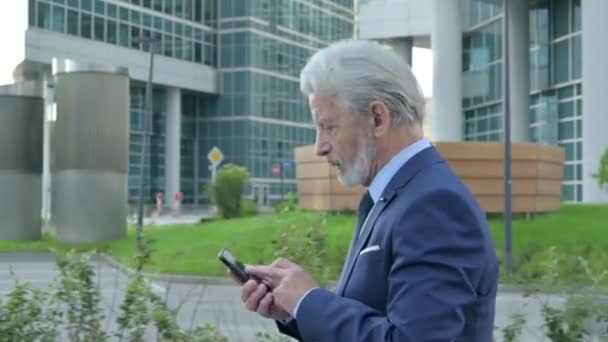 Alter Geschäftsmann mit Smartphone beim Gehen auf der Straße, Seitenlage — Stockvideo