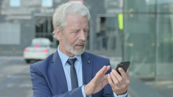 Oude zakenman viert feest op smartphone terwijl hij buiten staat — Stockvideo