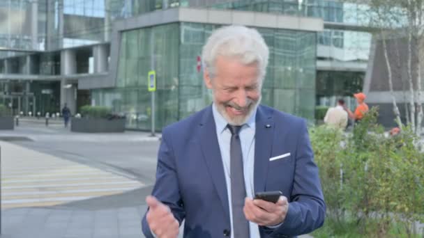 Stary Biznesmen świętuje sukces w telefonie podczas spaceru po ulicy — Wideo stockowe