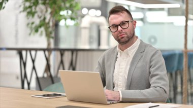 Dizüstü bilgisayarlı, Kameraya bakan Kafkasyalı bir genç.