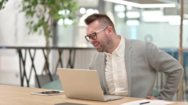 Hardwerkende blanke jongeman met laptop met rugpijn in kantoor — Stockfoto