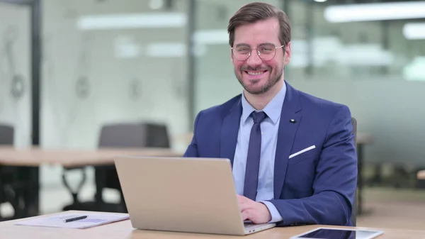 Ung affärsman med bärbar dator ler mot kameran i Office — Stockfoto