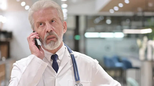 Porträt eines fröhlichen alten Arztes, der am Telefon spricht — Stockfoto
