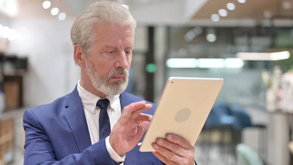 Portrait of focused Old Businessman using Digital Tablet