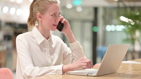 Zakenvrouw met laptop aan het telefoneren op kantoor — Stockfoto