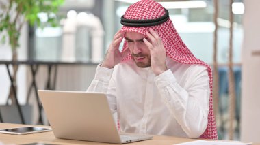 Dizüstü bilgisayarı olan stresli bir Arap İşadamı ofiste baş ağrısı çekiyor