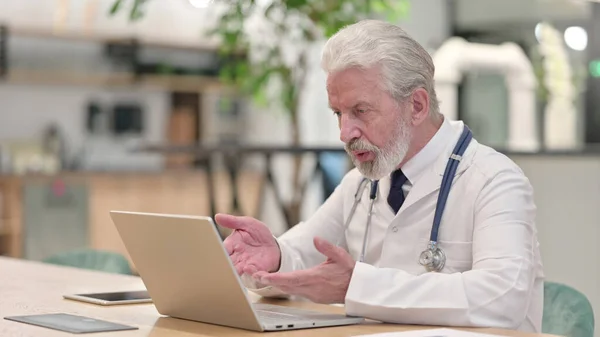 Velho médico conversando com o paciente através de chamada de vídeo no laptop — Fotografia de Stock