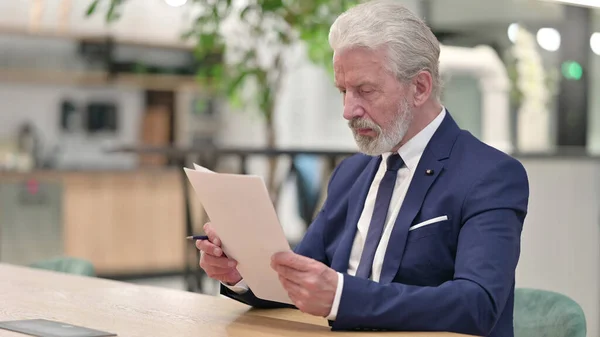 Vieil homme d'affaires concentré lisant des documents au bureau — Photo