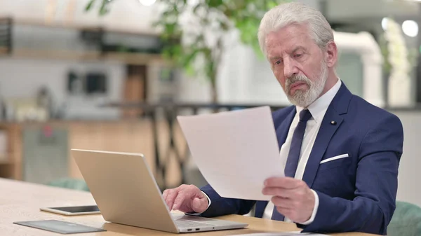 Ancien homme d'affaires avec ordinateur portable lecture de documents dans le bureau — Photo