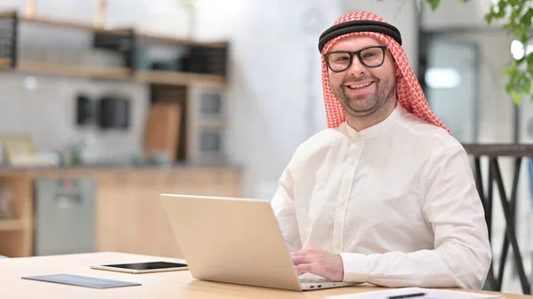 Dizüstü bilgisayarlı genç bir Arap Kameraya gülümsüyor — Stok fotoğraf