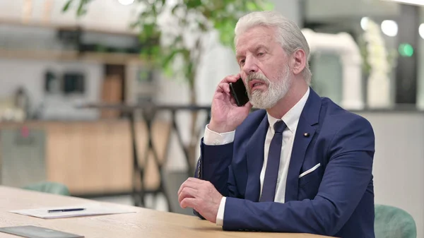 Viejo empresario alegre que habla por teléfono en la oficina —  Fotos de Stock