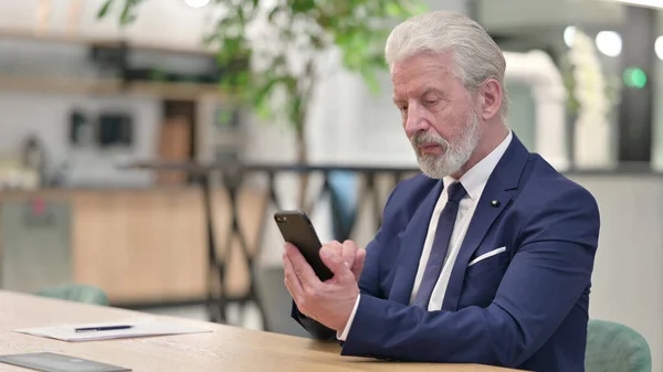 Old Businessman Browsing Internet na Smartphone v kanceláři — Stock fotografie