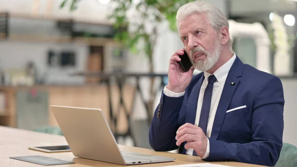 Starý podnikatel s notebookem mluví na telefonu — Stock fotografie